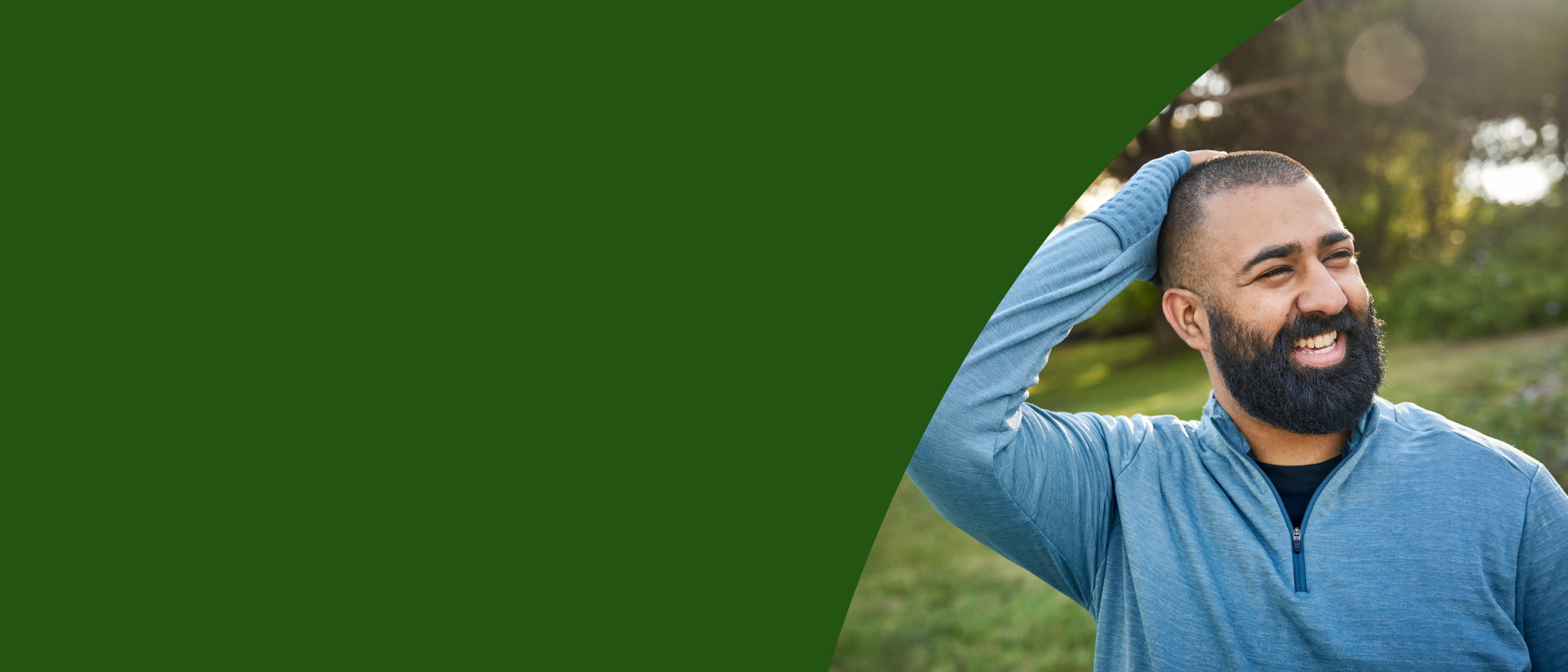 A smiling bearded man in a blue quarter-zip pullover shirt stands outdoors on a grassy lawn, with a large dark green graphic overlay covering the left side of the frame. - desktop
